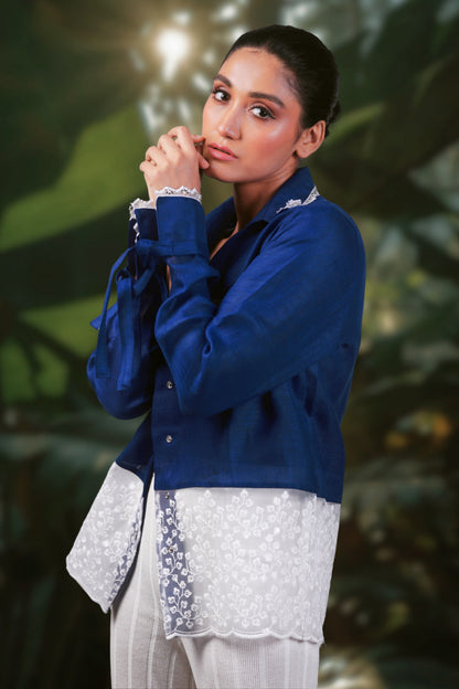 Model wearing a cobalt blue oversized crush shirt by 66aura, standing on a patterned carpet with props in the background.
